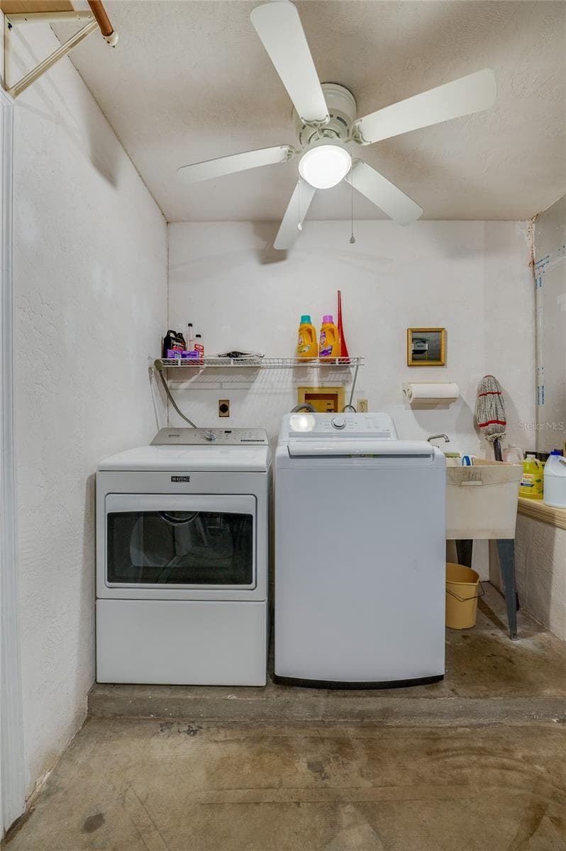 Dedicated laundry area equipped with a side-by-side washer and dryer, utility sink, overhead wire storage rack, and a ceiling fan. - 4669 SECRET RIVER TRL, PORT ORANGE