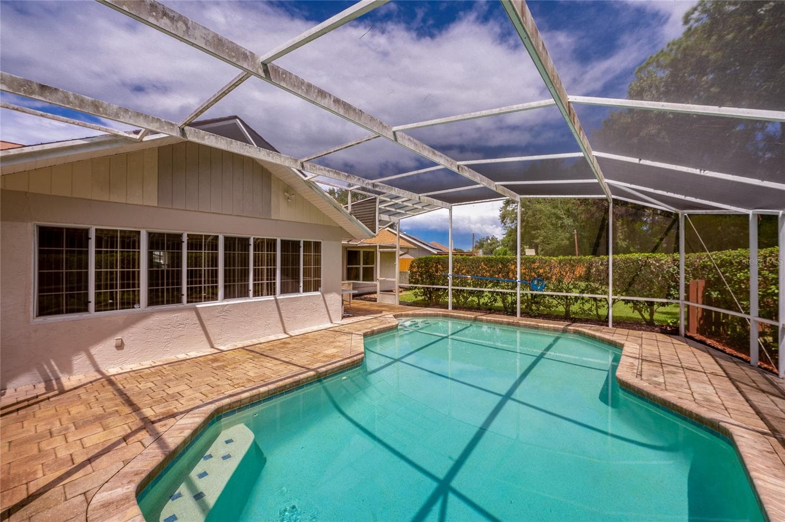 Alternate angle of the screened swimming pool enclosure, highlighting the extensive paved deck and home exterior. - 4669 SECRET RIVER TRL, PORT ORANGE