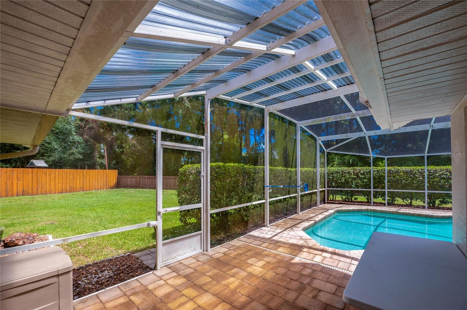 Paved patio area leading to a screened-in swimming pool enclosure with views of the grassy lawn. - 4669 SECRET RIVER TRL, PORT ORANGE