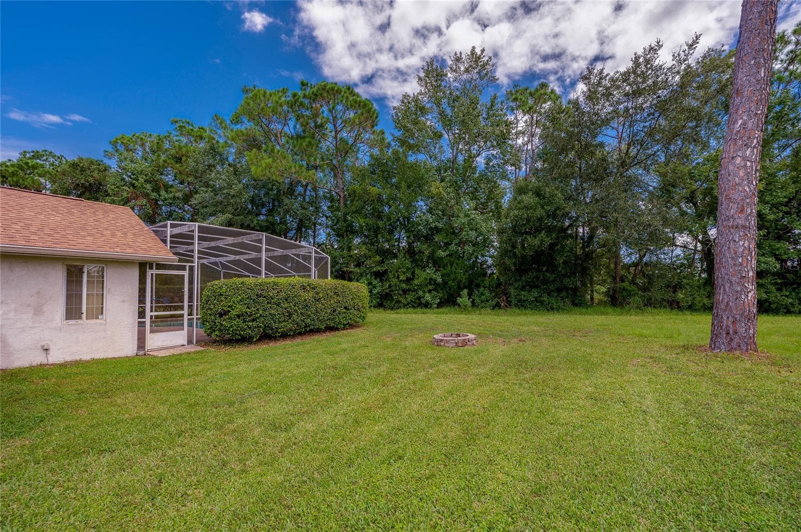 Expansive grassy backyard featuring a stone fire pit, mature trees, and a view of the pool enclosure. - 4669 SECRET RIVER TRL, PORT ORANGE