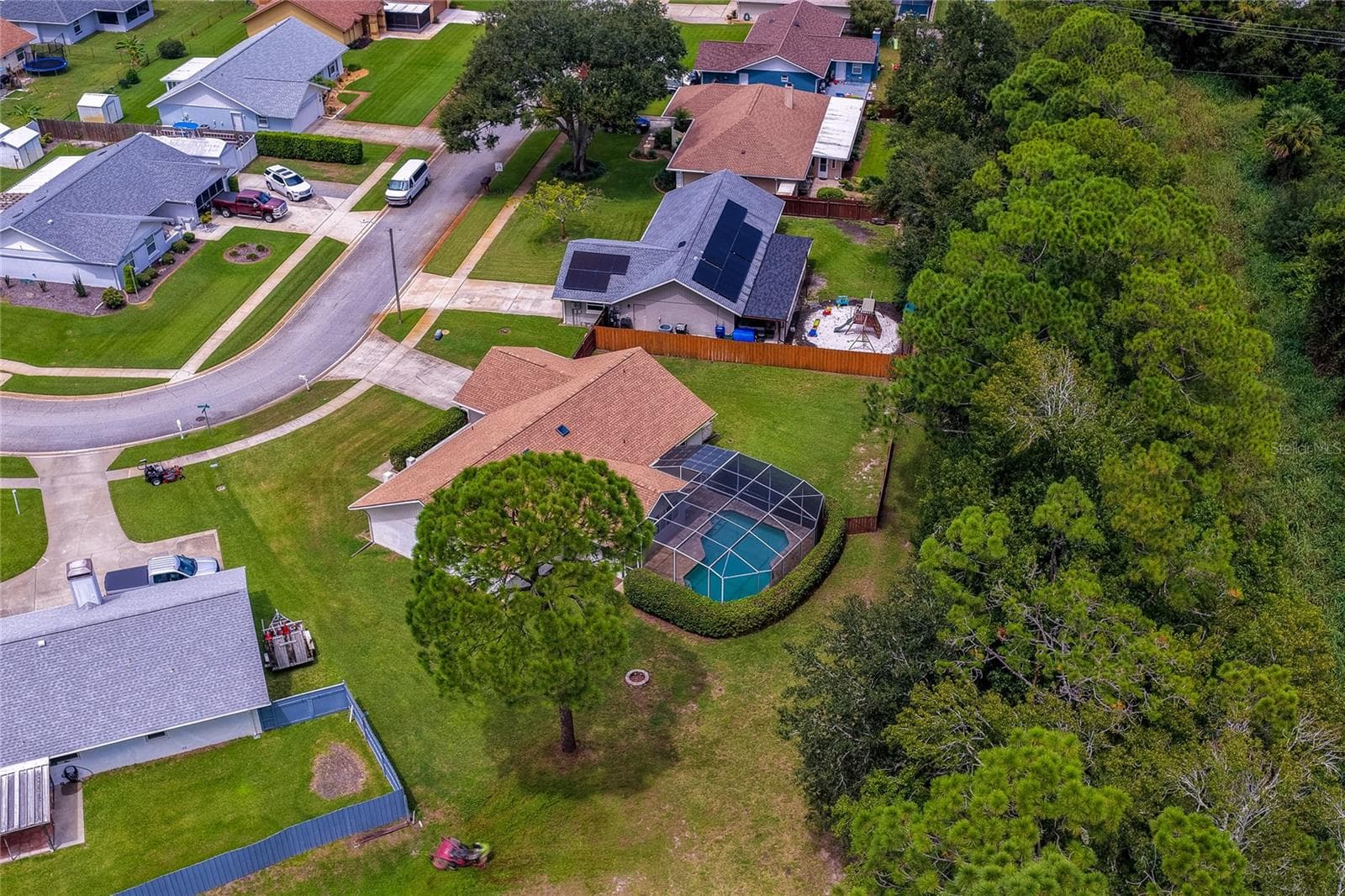 Bird’s-eye view focusing on the backyard pool structure, large lawn, and dense tree-lined privacy buffer. - 4669 SECRET RIVER TRL, PORT ORANGE