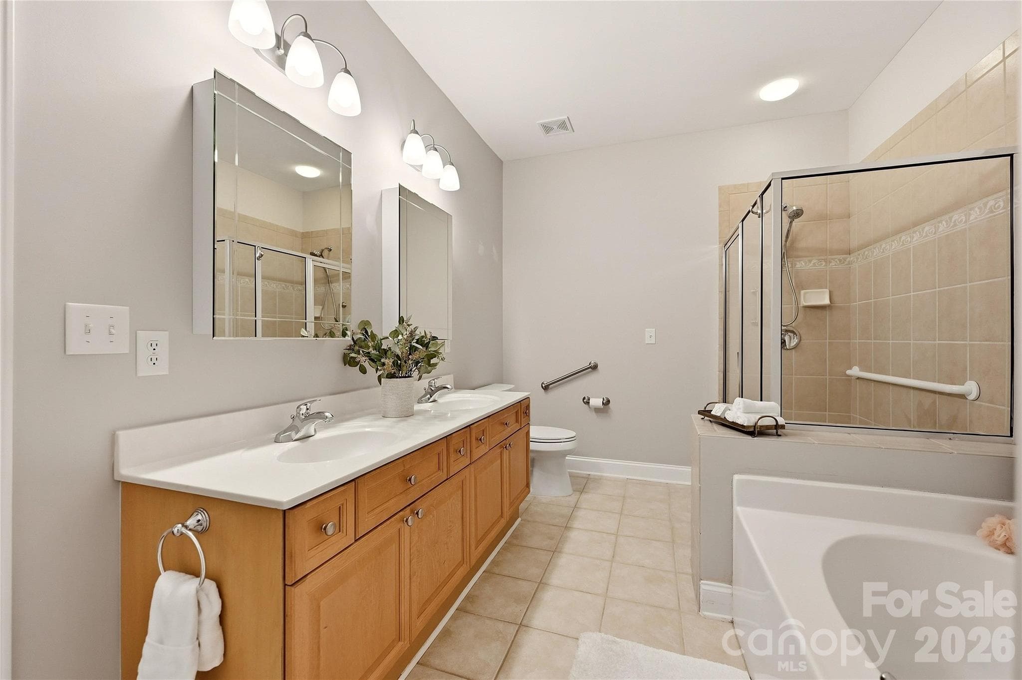 Primary bathroom features a long dual-sink vanity, tile flooring, garden tub, separate shower, and accessibility grab bars. - 9009 Rosalyn Glen Road, Cornelius