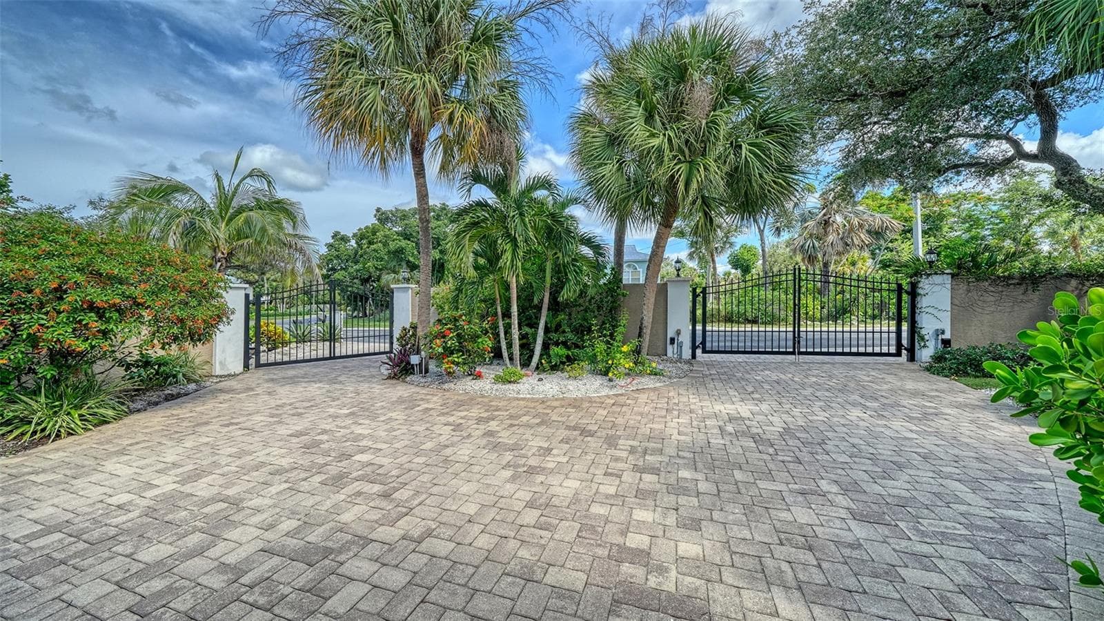 Circular paver driveway and gated entrance framed by mature palms and tropical landscaping. - SARASOTA