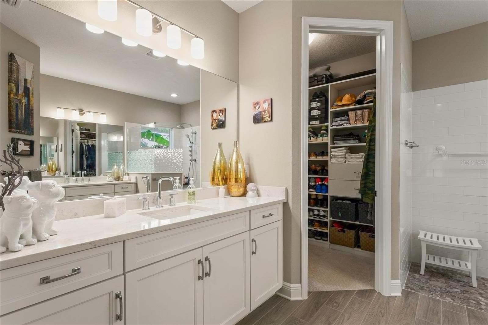 Primary bathroom with two individual sink vanities—one on each side—featuring modern cabinetry, a spacious walk-in shower, contemporary tile flooring, and direct access to a custom-designed walk-in closet consistent with the thoughtfully crafted closets and pantries found throughout the home. - 10625 FALLING LEAF CT, PARRISH