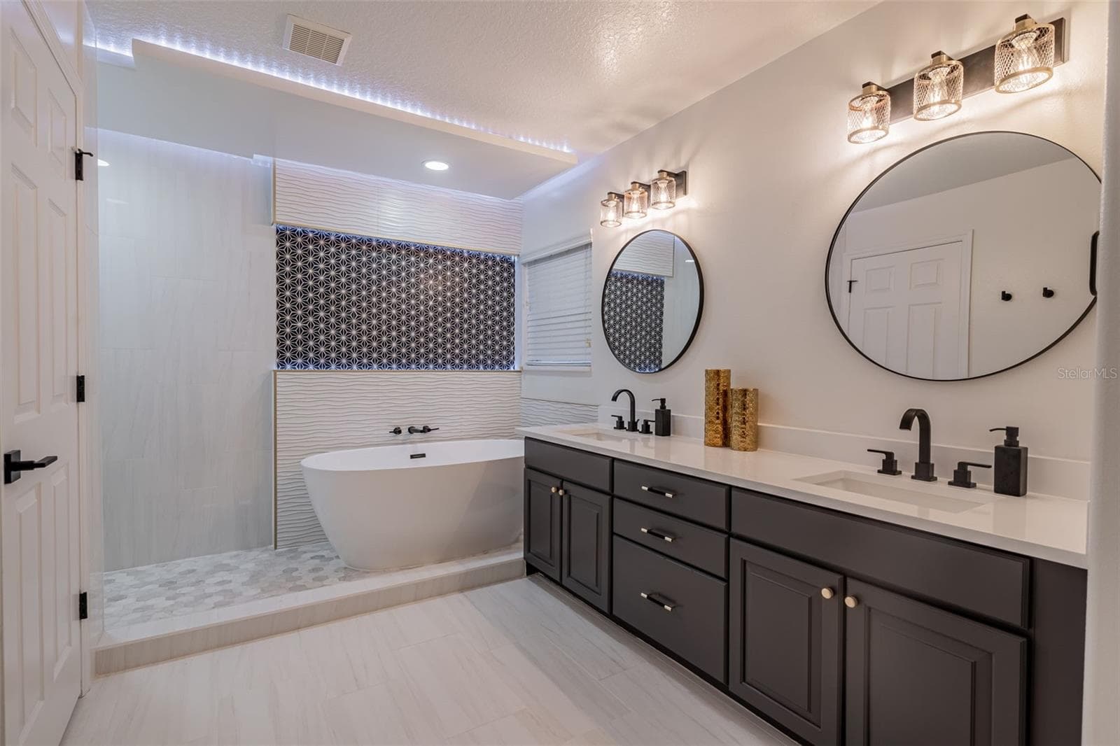 Completely gutted and rebuilt in 2022 with an investment of approximately $32,000, the primary bathroom includes a floating quartz double vanity, illuminated mirrors, an oversized walk in rain shower, multiple shower fixtures and lighted niches. - 14585 CHEEVER ST, ORLANDO