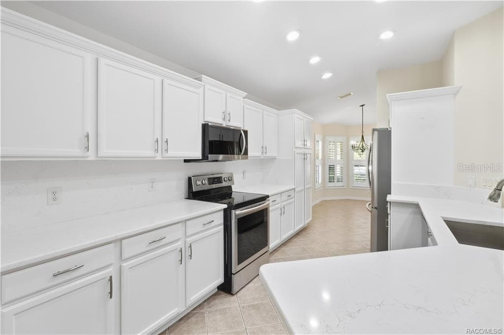 KITCHEN – Clean, bright finishes define the remodeled kitchen with white raised-panel cabinetry, modern hardware, quartz countertops & backsplash, stainless-steel range and built-in microwave. Recessed lighting keeps the workspace bright. - 6410 W CANNONDALE DR, CRYSTAL RIVER