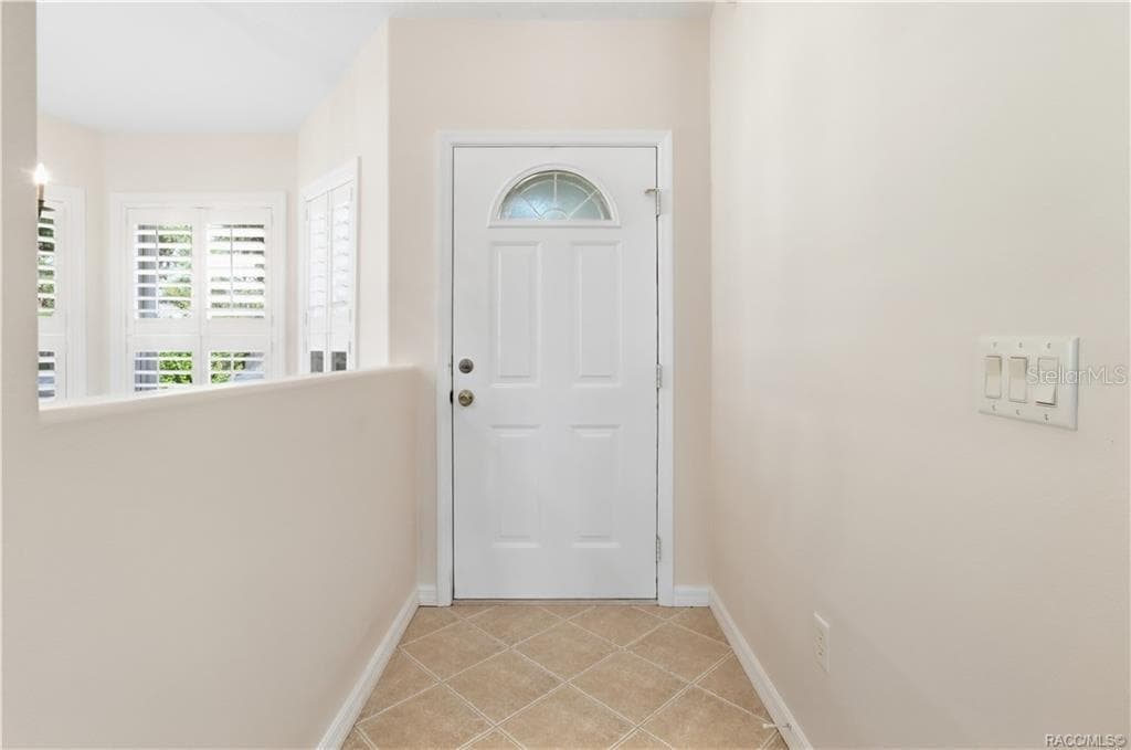 FOYER – Bright entry foyer with neutral tile flooring laid on the diagonal, crisp white trim & a front door featuring a decorative half-moon glass insert. Plantation shutters on the adjacent windows add both style & light control. - 6410 W CANNONDALE DR, CRYSTAL RIVER