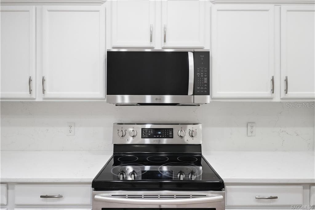 APPLIANCE DETAIL – Close-up of the stainless-steel electric range and microwave hood surrounded by crisp white cabinetry, quartz countertops & coordinating backsplash for a fresh, modern presentation. - 6410 W CANNONDALE DR, CRYSTAL RIVER