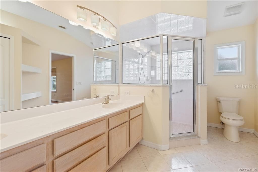 PRIMARY BATHROOM – Wider view showcasing the dual-sink vanity, oversized mirror, glass-enclosed walk-in shower, tile flooring & separate toilet area. - 6410 W CANNONDALE DR, CRYSTAL RIVER