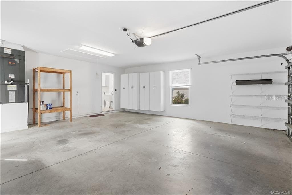 2-CAR GARAGE / STORAGE – Alternate garage view showcasing additional storage with wall-mounted cabinets, wire shelving, freestanding shelving & access to the interior laundry room. - 6410 W CANNONDALE DR, CRYSTAL RIVER