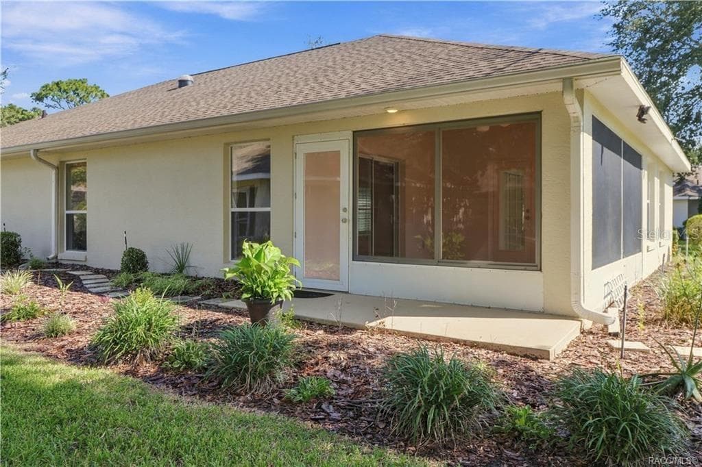 REAR EXTERIOR / SUNROOM – Exterior view of the enclosed sunroom with screened/windowed walls, exterior access & surrounding landscaped beds. - 6410 W CANNONDALE DR, CRYSTAL RIVER
