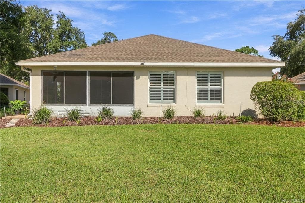REAR EXTERIOR – Full rear elevation showcasing the enclosed sunroom, additional rear windows with plantation shutters, mature landscaping & spacious green lawn. - 6410 W CANNONDALE DR, CRYSTAL RIVER