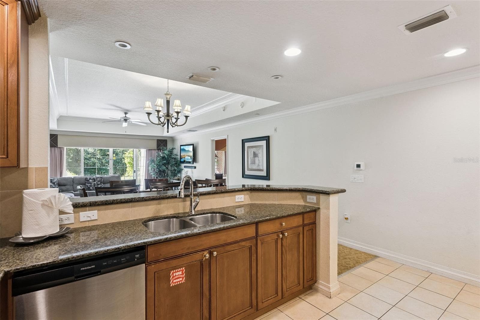 Kitchen Pass-Through Counter: Functional kitchen layout with rich wood cabinetry, durable granite countertops, an undermount double sink, and open views into the living space. - 7656 WHISPER WAY #102, REUNION