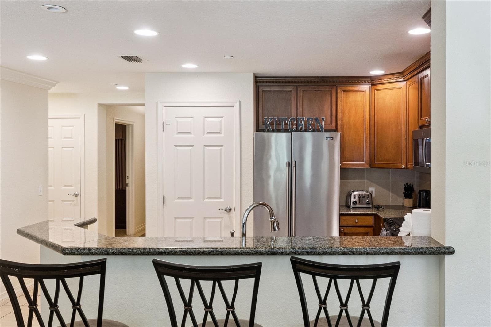 Breakfast Bar & Kitchen: Raised granite breakfast bar ideal for casual seating, featuring a stainless steel refrigerator, recessed lighting, and a pantry door. - 7656 WHISPER WAY #102, REUNION