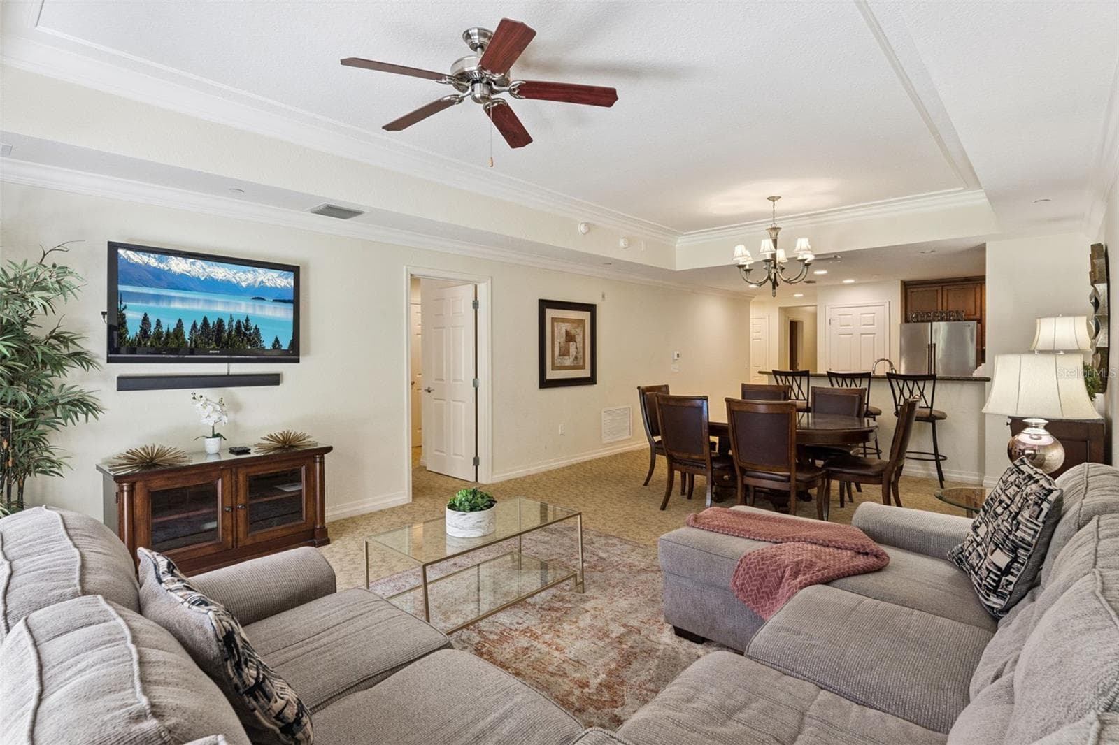 Open-Concept Layout: Spacious living and dining combination area seamlessly connecting to the kitchen, complete with tray ceiling accents and ceiling fans. - 7656 WHISPER WAY #102, REUNION