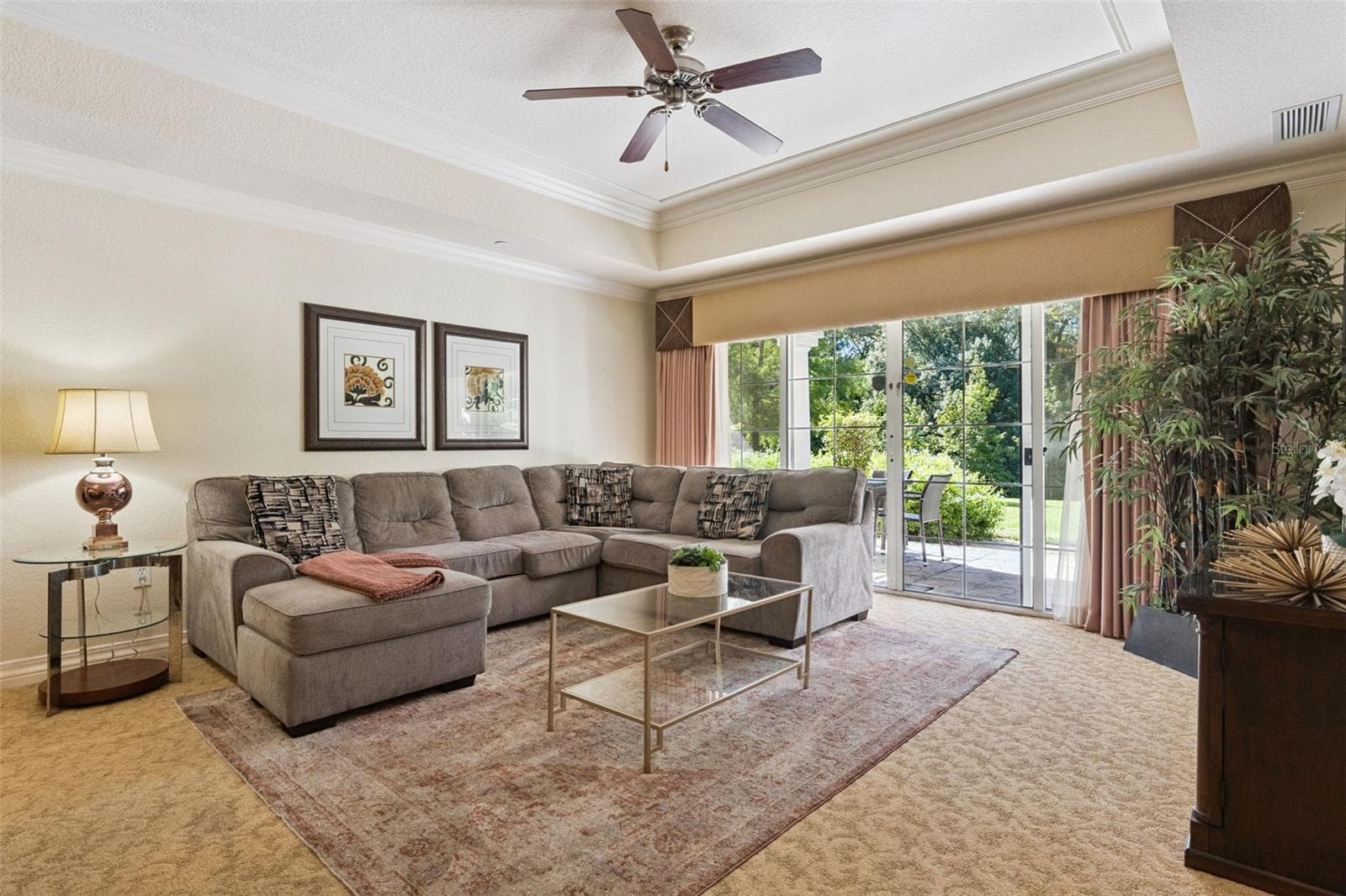 Living Room: Bright living space boasting tray ceilings, plush carpeting, a ceiling fan, and sliding glass doors opening to outdoor greenery views. - 7656 WHISPER WAY #102, REUNION