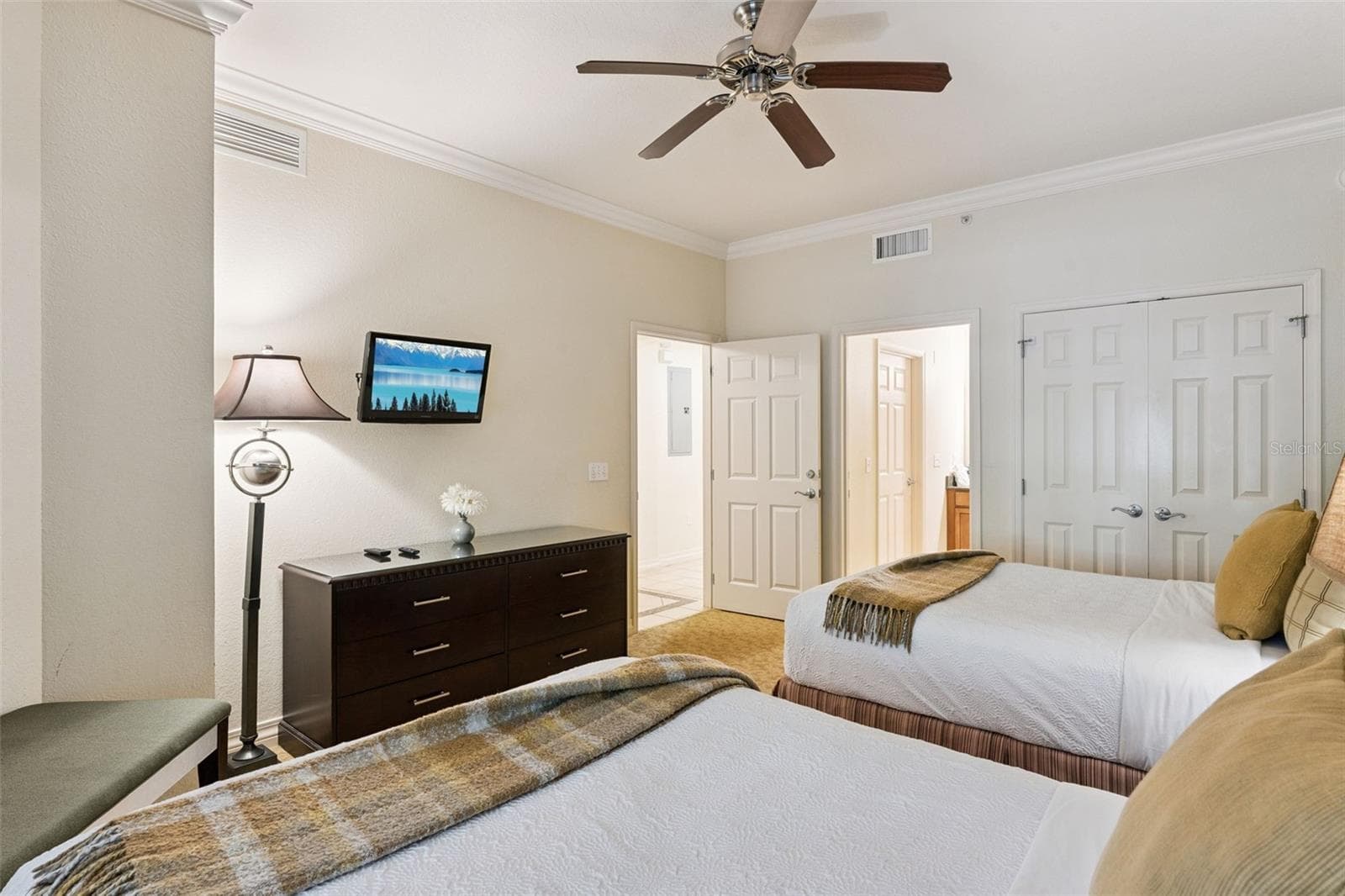 Double Bedroom Alternate View: Angle of the double guest room showcasing a matching dresser, wall-mounted TV, double bi-fold closet doors, and adjacent hallway access. - 7656 WHISPER WAY #102, REUNION