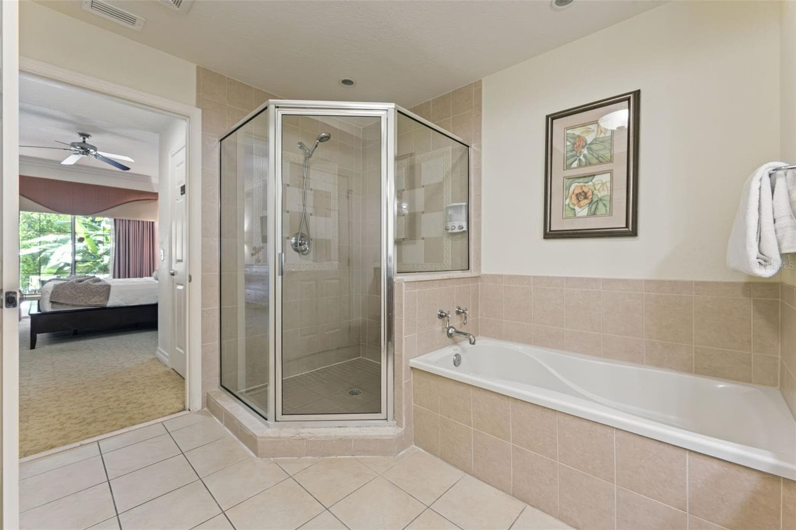 Primary Bathroom & Soaking Tub: Ensuite primary bath equipped with a glass-framed corner walk-in shower, separate soaking tub with neutral tile surround, and tile flooring. - 7656 WHISPER WAY #102, REUNION