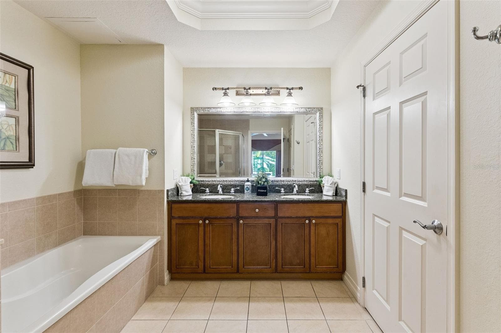 Primary Bathroom Double Vanity: Primary suite vanity featuring dual undermount sinks, rich wood cabinetry, granite counters, decorative framed mirror, and an updated vanity light bar. - 7656 WHISPER WAY #102, REUNION