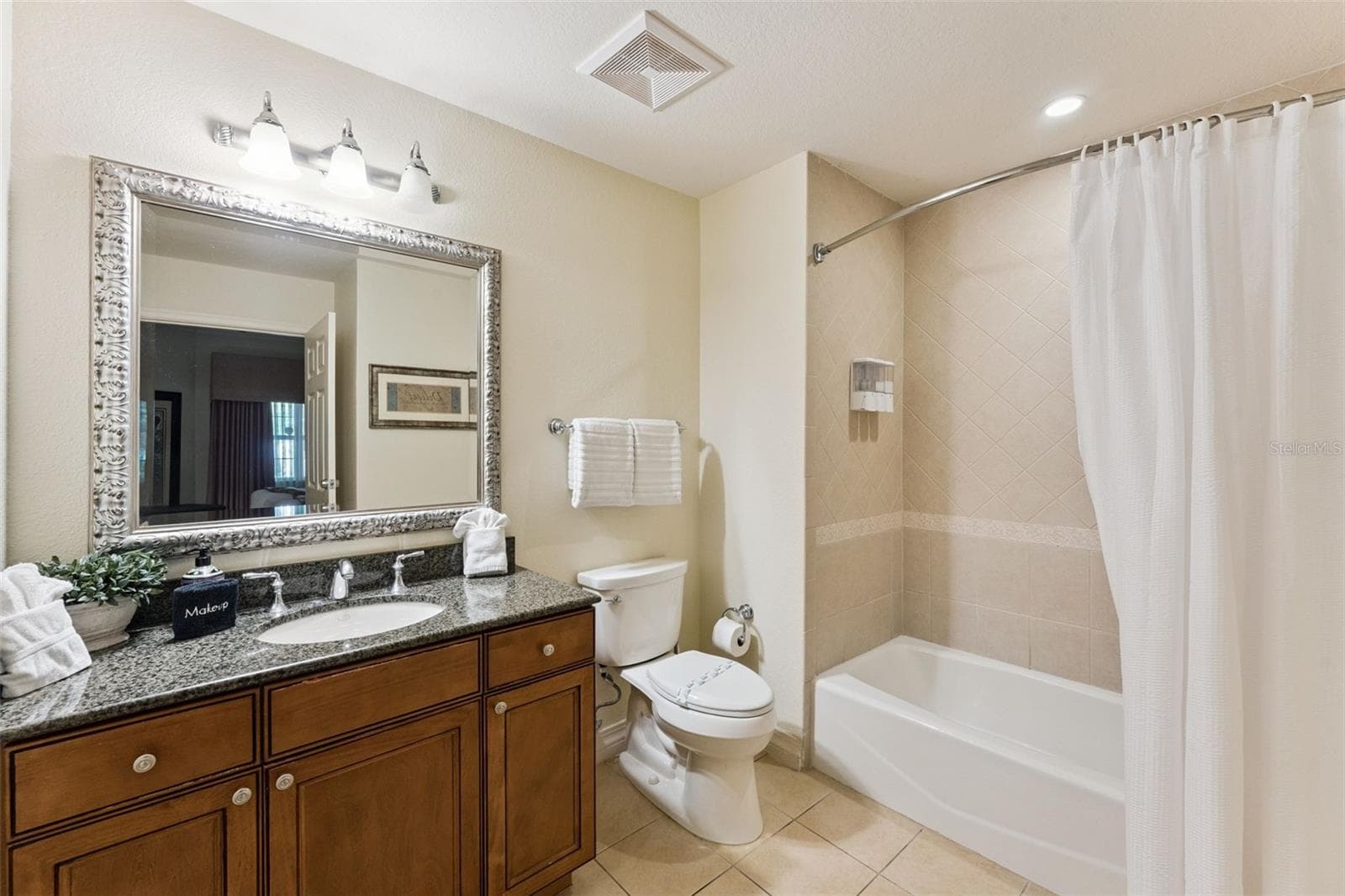 Second Full Bathroom: Guest bathroom featuring a wood vanity with granite countertop, decorative framed mirror, toilet, and tiled shower/tub combination. - 7656 WHISPER WAY #102, REUNION