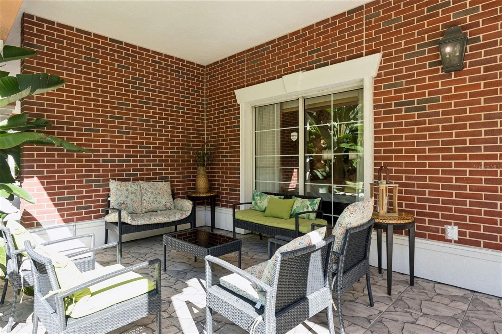 Covered Outdoor Patio: Expansive covered outdoor patio featuring classic red brick accent walls, stone-patterned tile flooring, sliding door access, and ample space for lounge seating. - 7656 WHISPER WAY #102, REUNION