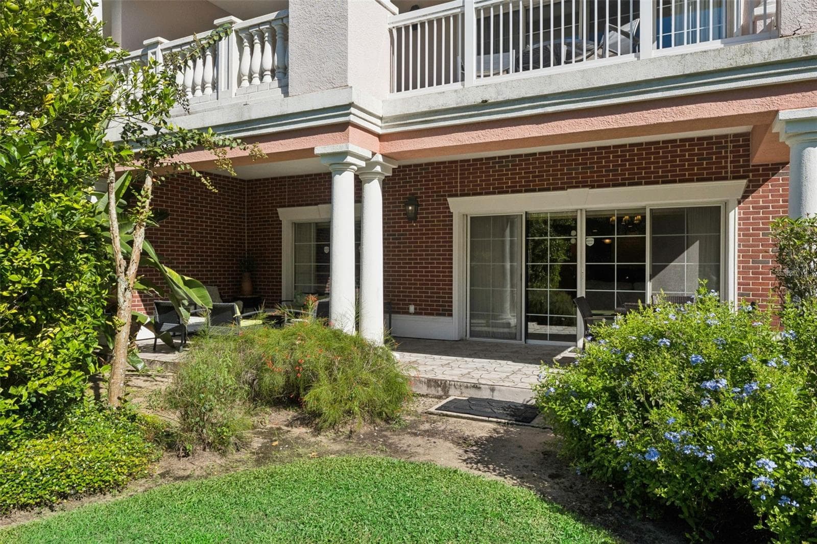 Ground-Floor Exterior & Patio: Ground-floor exterior view showcasing the unit's private covered patio, brick accents, sliding glass entry, and surrounding flower beds. - 7656 WHISPER WAY #102, REUNION