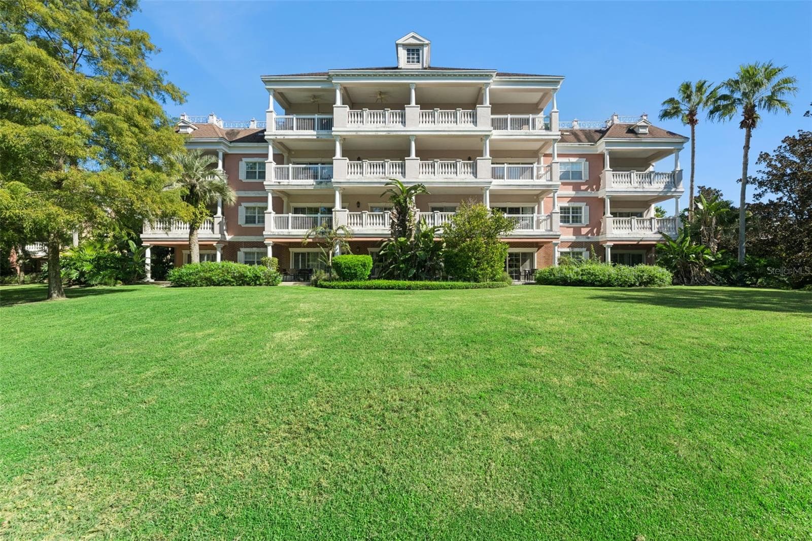 Rear Building Elevation: Full rear elevation view of the multi-story condominium building featuring multi-tiered covered balconies, a sweeping green lawn, and tropical landscaping. - 7656 WHISPER WAY #102, REUNION