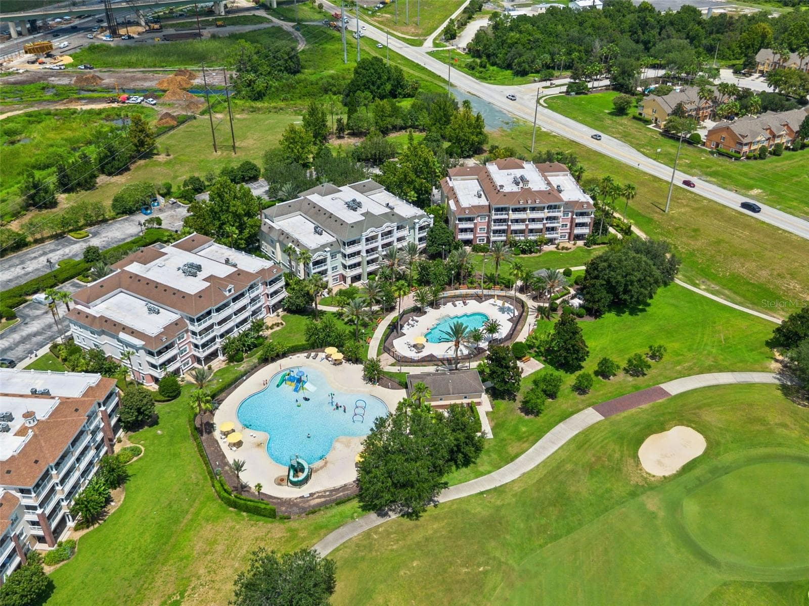 Resort Community Aerial: High-angle aerial view displaying the resort pool complex, multi-story condo buildings, resident parking, and adjoining golf course fairway. - 7656 WHISPER WAY #102, REUNION