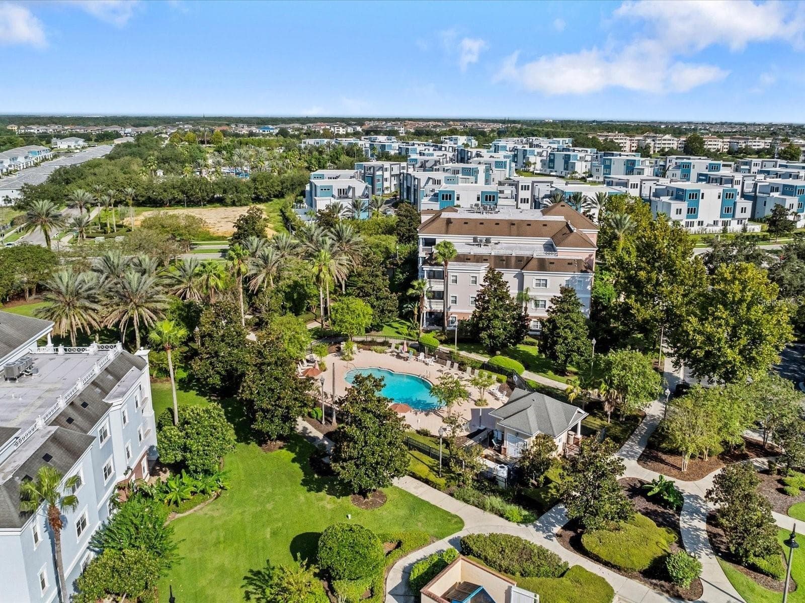Neighborhood Pool & Grounds Aerial: High-angle aerial view of the neighborhood pool, paved walking trails, lush green spaces, and surrounding multi-story condo buildings. - 7656 WHISPER WAY #102, REUNION