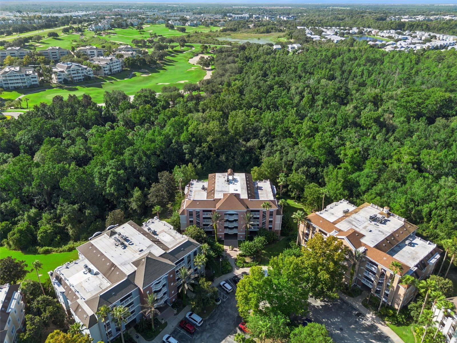 Overhead Conservation View: Overhead drone perspective highlighting the secluded setting of the residential buildings surrounded by dense tree canopy and neighboring golf greens. - 7656 WHISPER WAY #102, REUNION