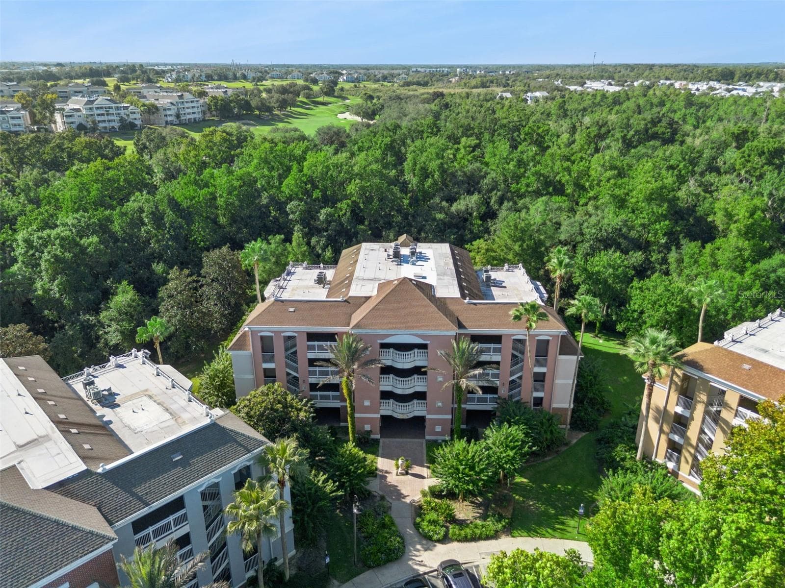Building Exterior Aerial: Focused aerial shot highlighting the Mediterranean-style building facade, covered central entryway, tropical palm landscaping, and mature tree canopy. - 7656 WHISPER WAY #102, REUNION