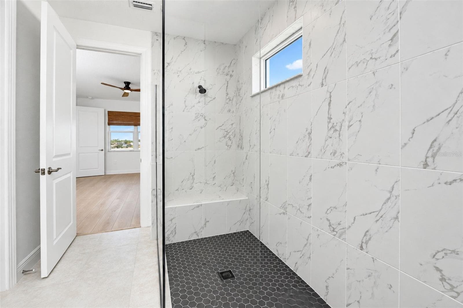 Luxurious oversized walk-in shower featuring floor-to-ceiling marble-look tile, frameless glass, contrasting mosaic tile floor and built-in bench. - 237 VISTERA BLVD, NOKOMIS