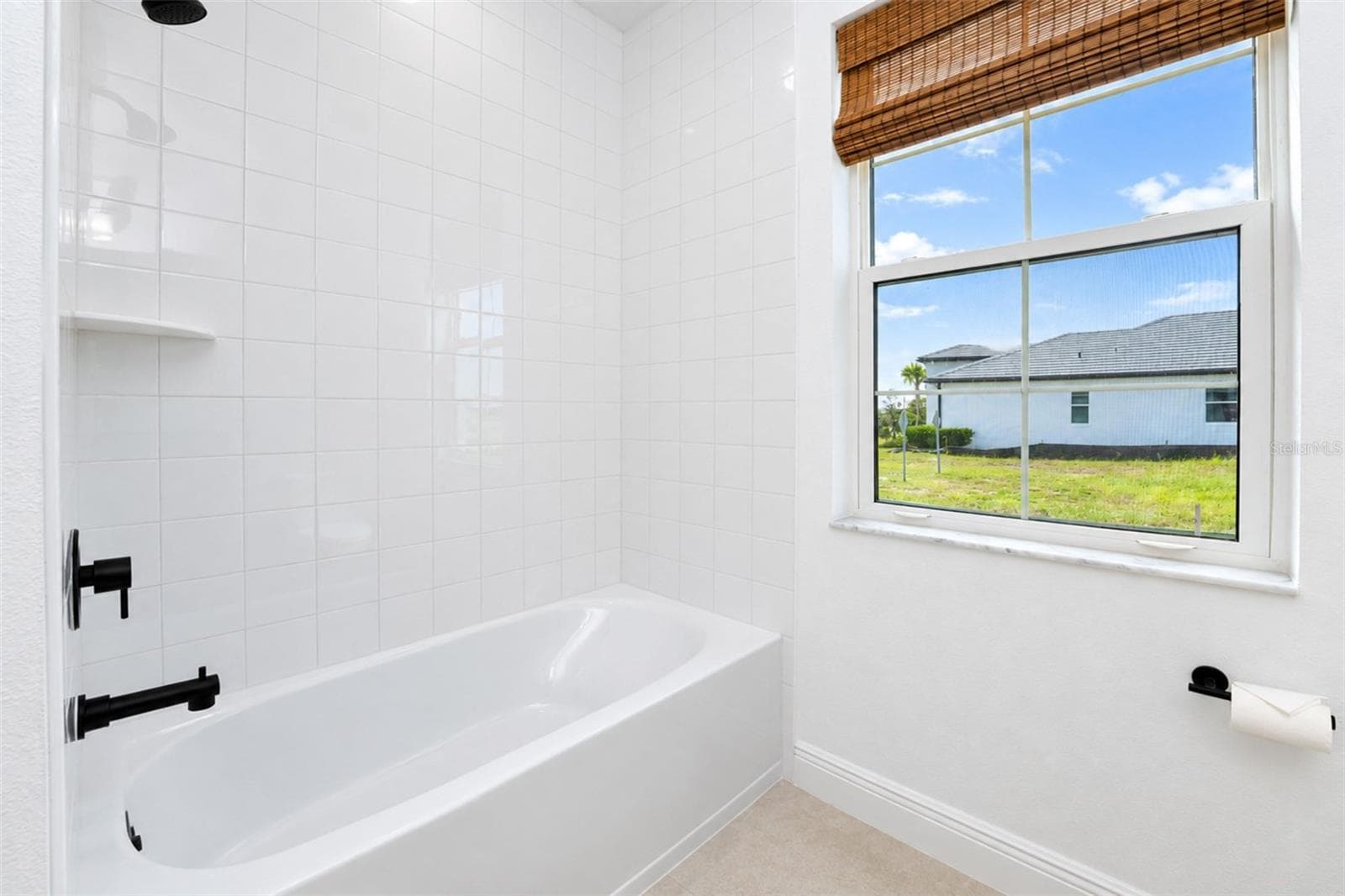 Tub/shower combination with crisp white tile extending to the ceiling and contrasting matte-black fixtures. - 237 VISTERA BLVD, NOKOMIS