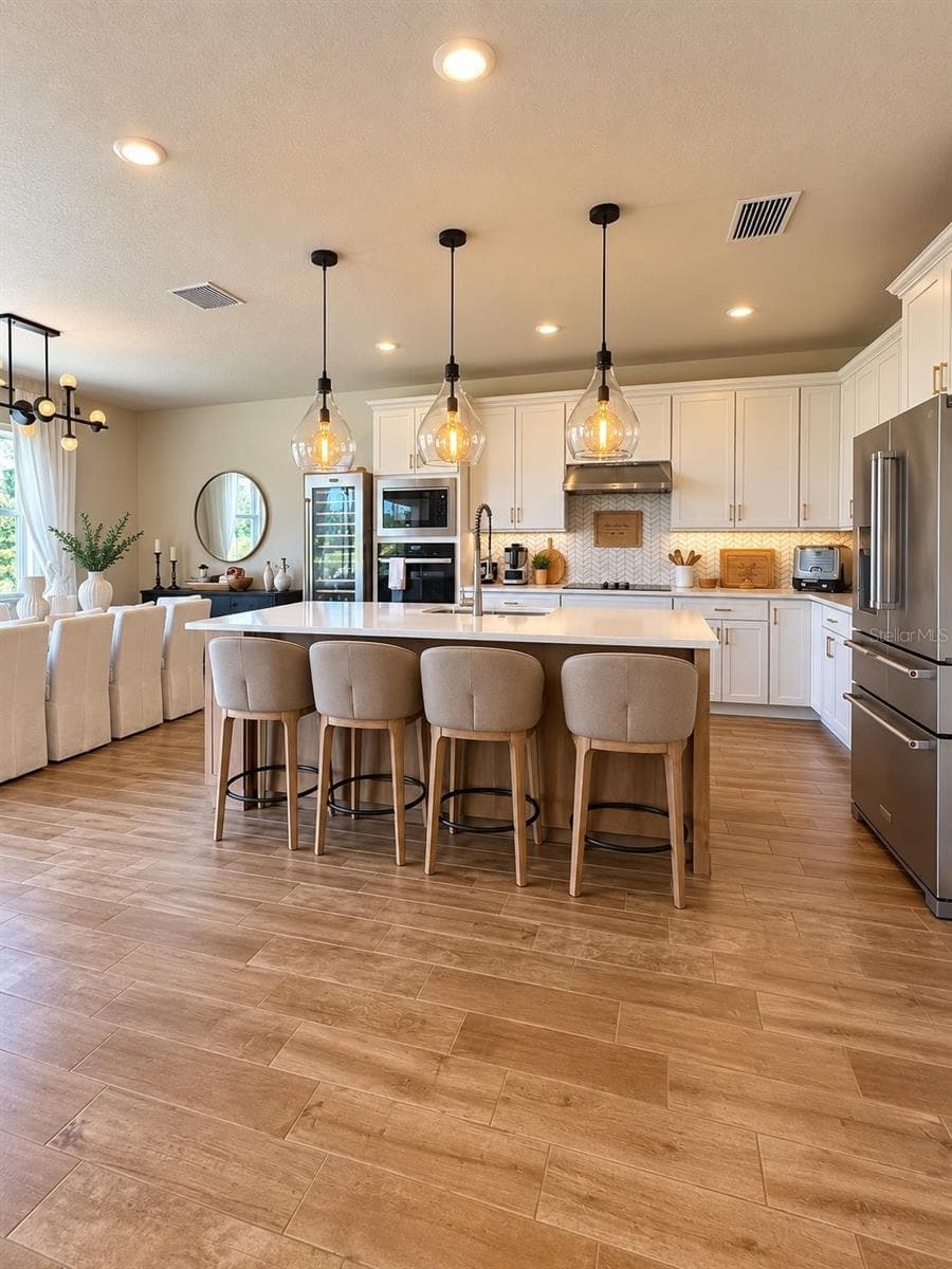 Spacious gourmet kitchen featuring a large center island with seating, quartz countertops, abundant cabinetry, stainless steel appliances, and an open-concept layout ideal for entertaining. - 6735 REVERIE PARK AVE, ORLANDO