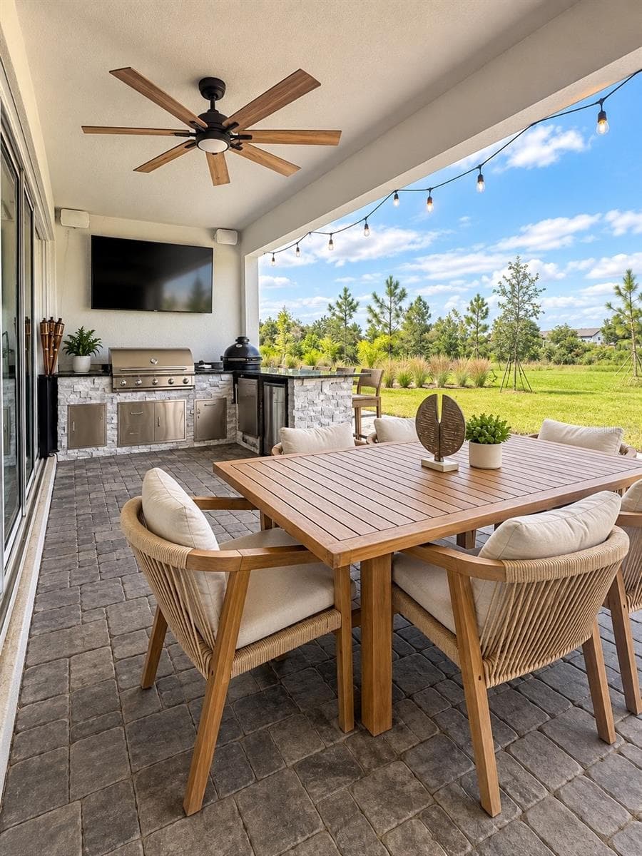 Covered outdoor living area with built-in kitchen, dining space, TV, ceiling fan, and peaceful backyard views—perfect for entertaining and enjoying the Florida lifestyle. - 6735 REVERIE PARK AVE, ORLANDO