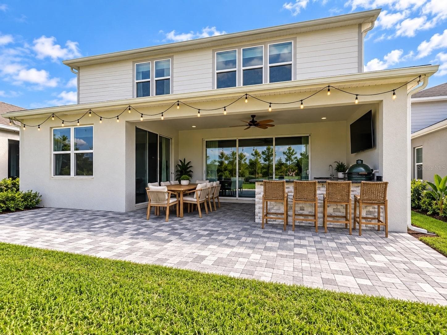 Spacious covered lanai with outdoor kitchen, bar seating, dining area, TV, and extended paver patio overlooking the backyard—ideal for year-round Florida outdoor living and entertaining. - 6735 REVERIE PARK AVE, ORLANDO