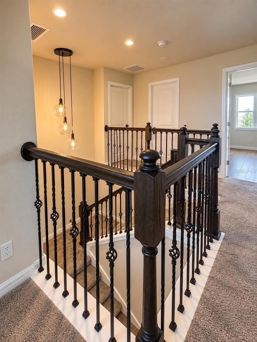 Second-Floor Landing – Elegant staircase with upgraded wood railing, decorative iron balusters, and modern pendant lighting - 6735 REVERIE PARK AVE, ORLANDO