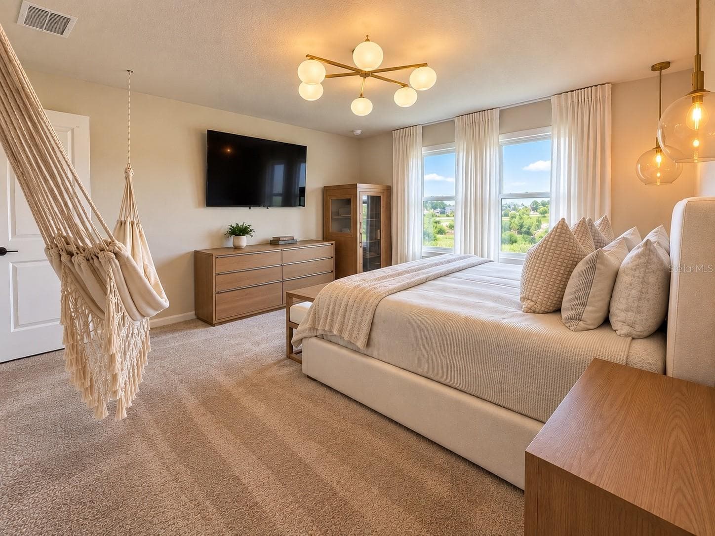 Expansive primary suite filled with natural light, featuring multiple windows with peaceful green views, plush carpeting, contemporary lighting, and generous space for a king-size bed and additional furnishings. A bright and inviting private retreat. - 6735 REVERIE PARK AVE, ORLANDO