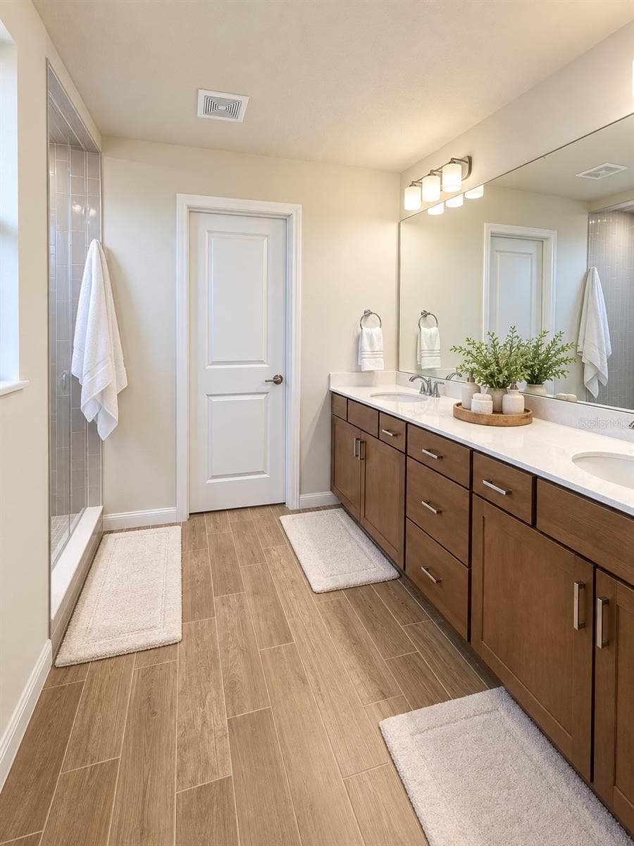 Primary Bathroom: Spacious primary bath featuring an extended dual-sink vanity with abundant cabinetry and counter space, a large wall-to-wall mirror, separate walk-in shower, and wood-look tile flooring. Bright, functional, and beautifully appointed - 6735 REVERIE PARK AVE, ORLANDO