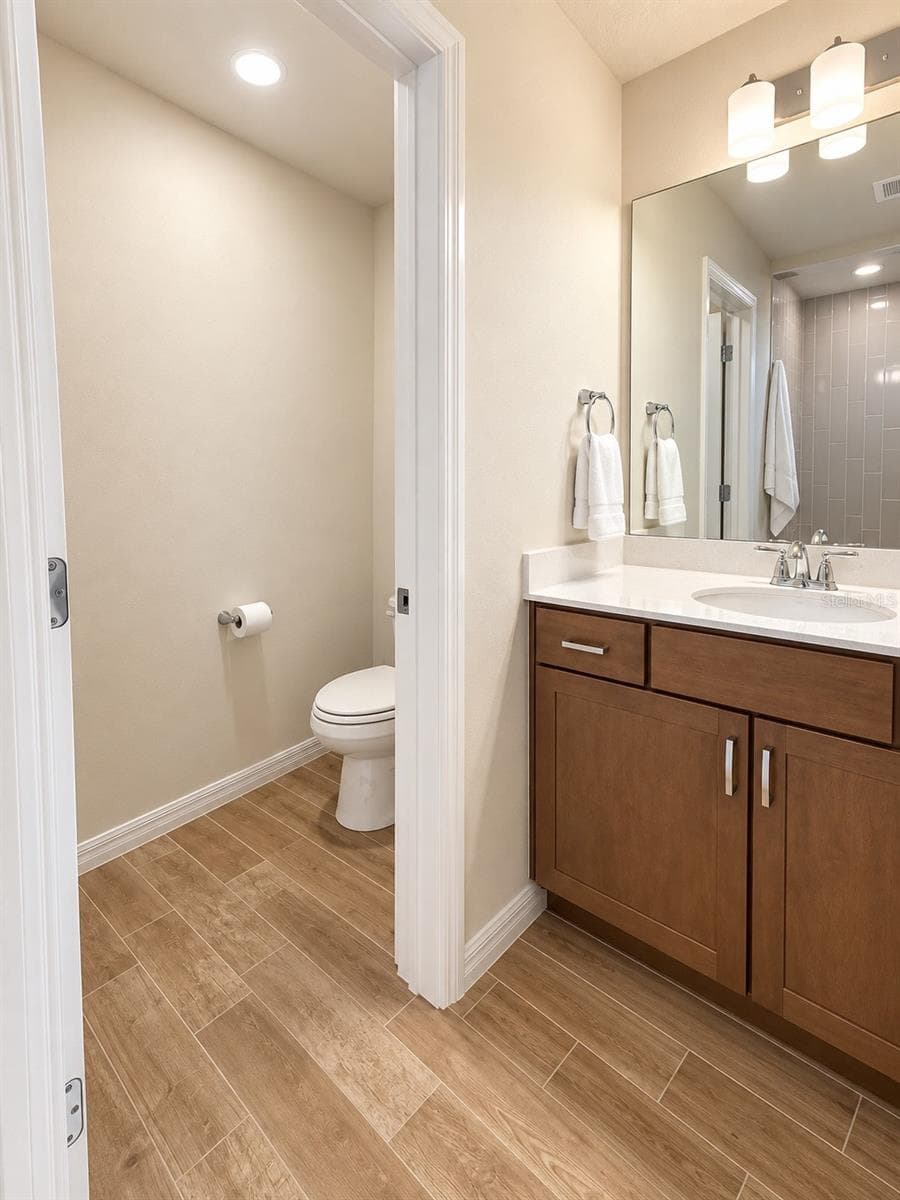 Spacious primary bath featuring a large vanity with quartz countertop, expansive wall-to-wall mirror, abundant cabinetry and a private water closet. Wood-look porcelain tile flooring adds warmth and durability to the space - 6735 REVERIE PARK AVE, ORLANDO