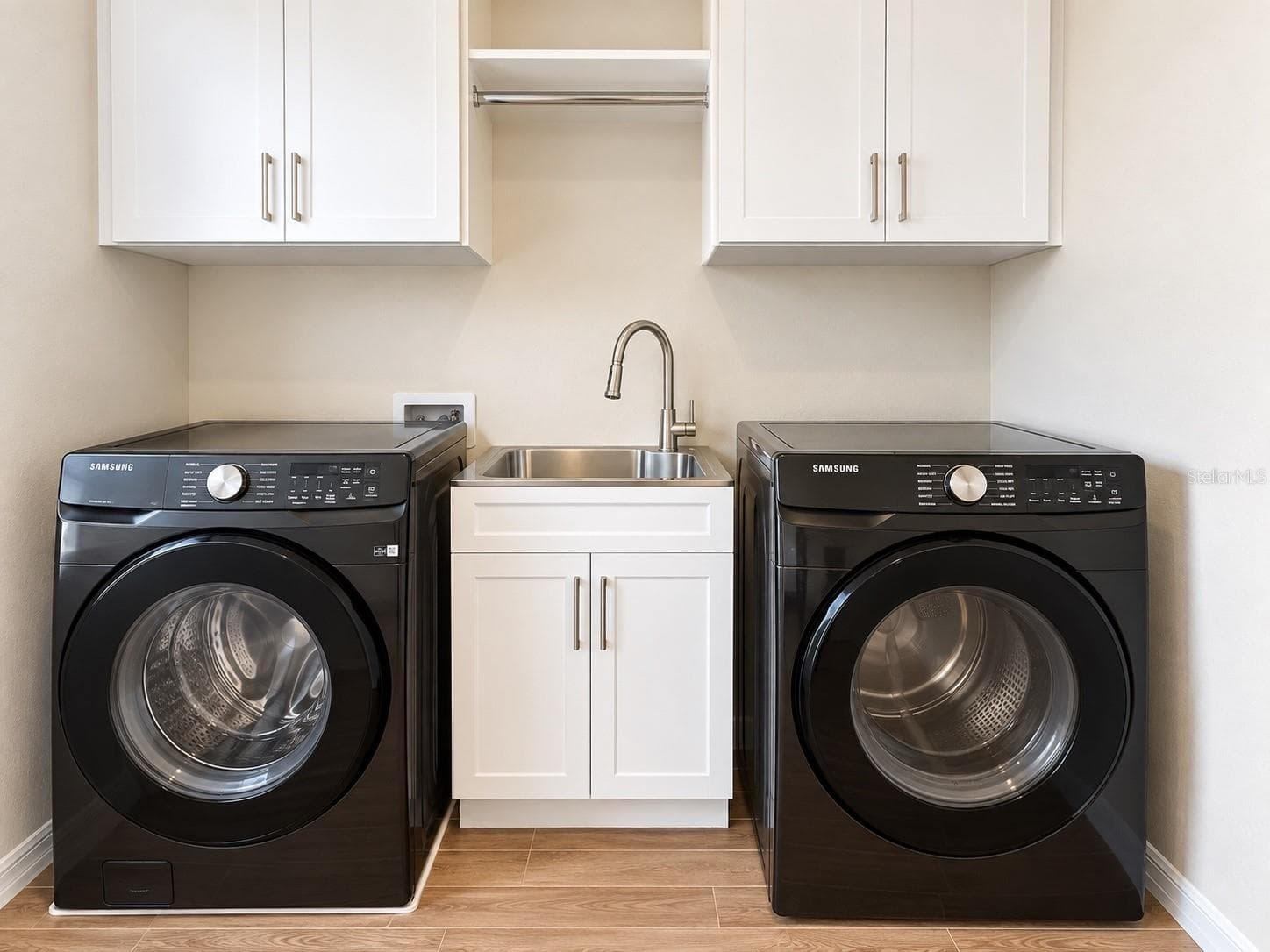 Spacious and functional laundry room featuring Samsung front-load washer and dryer, utility sink, ample built-in cabinetry, generous countertop workspace, and additional storage. Designed for convenience, organization, and everyday functionality. - 6735 REVERIE PARK AVE, ORLANDO