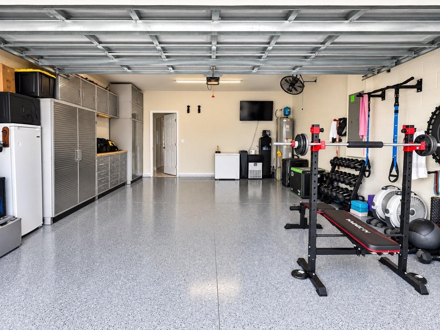 Oversized two-car garage with epoxy flooring, extensive built-in storage, organized workspace, and versatile home gym setup. - 6735 REVERIE PARK AVE, ORLANDO