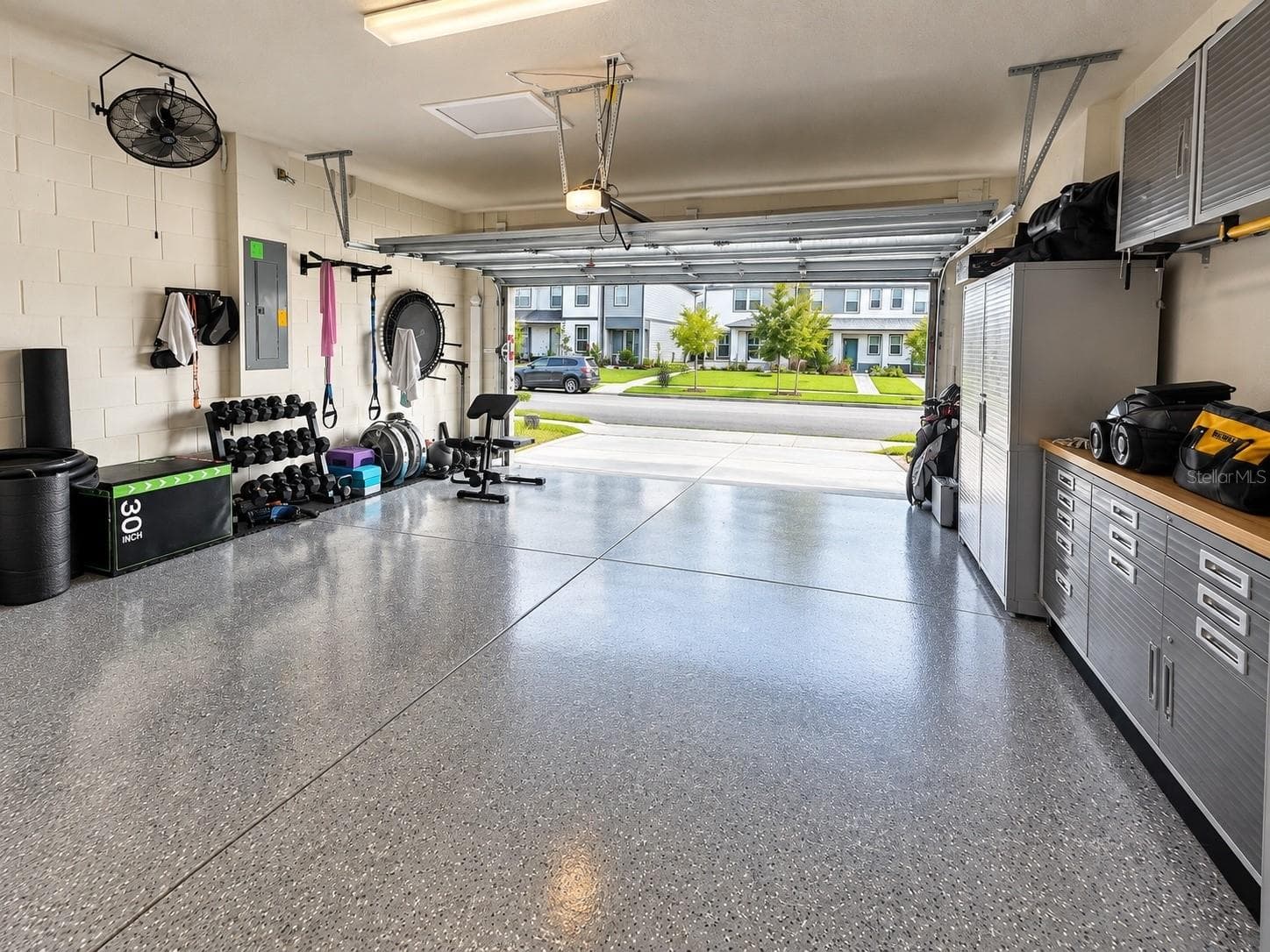 Spacious two-car garage featuring a durable epoxy-finished floor, built-in storage cabinetry, and dedicated fitness area. - 6735 REVERIE PARK AVE, ORLANDO