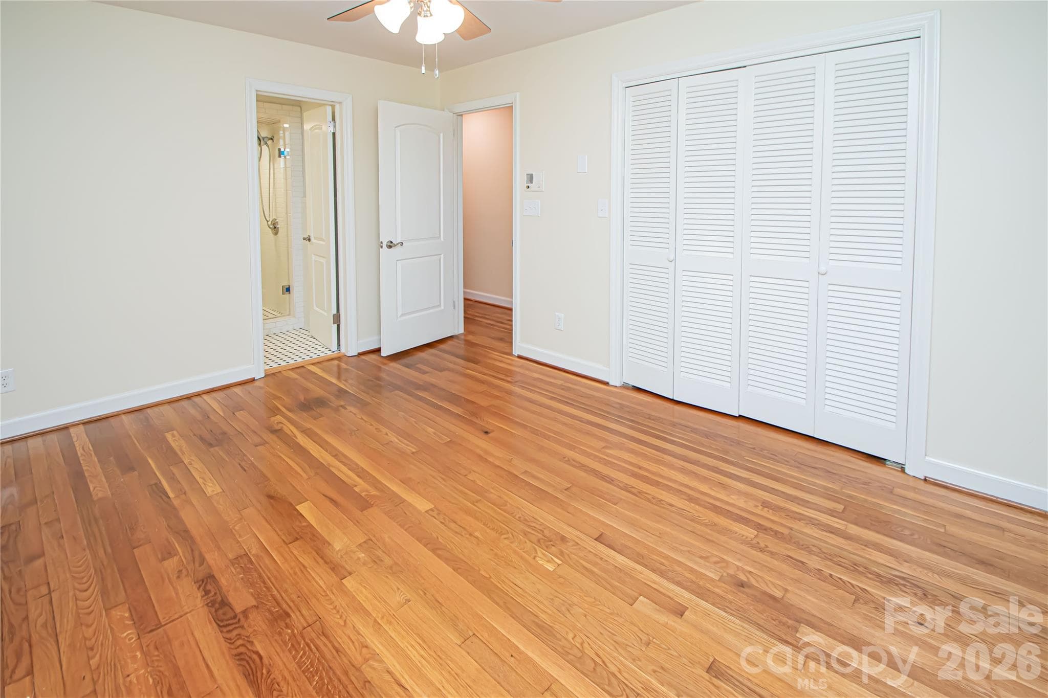 Spacious primary bedroom featuring beautiful hardwood flooring, a ceiling fan for climate control, and a generously sized closet. - 7400 Oakwood Lane, Charlotte