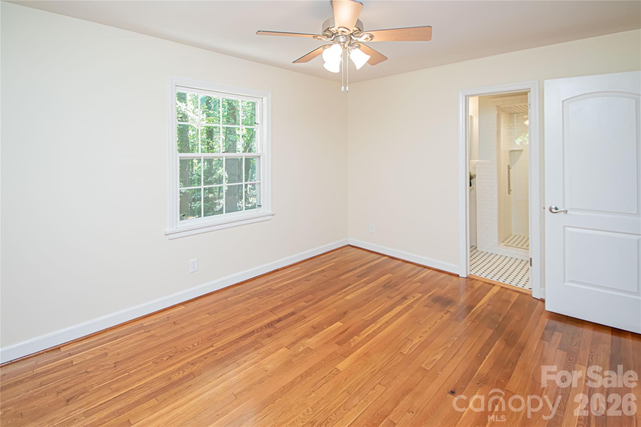 Spacious primary bedroom featuring beautiful hardwood flooring, a ceiling fan for climate control, and a generously sized closet. - 7400 Oakwood Lane, Charlotte