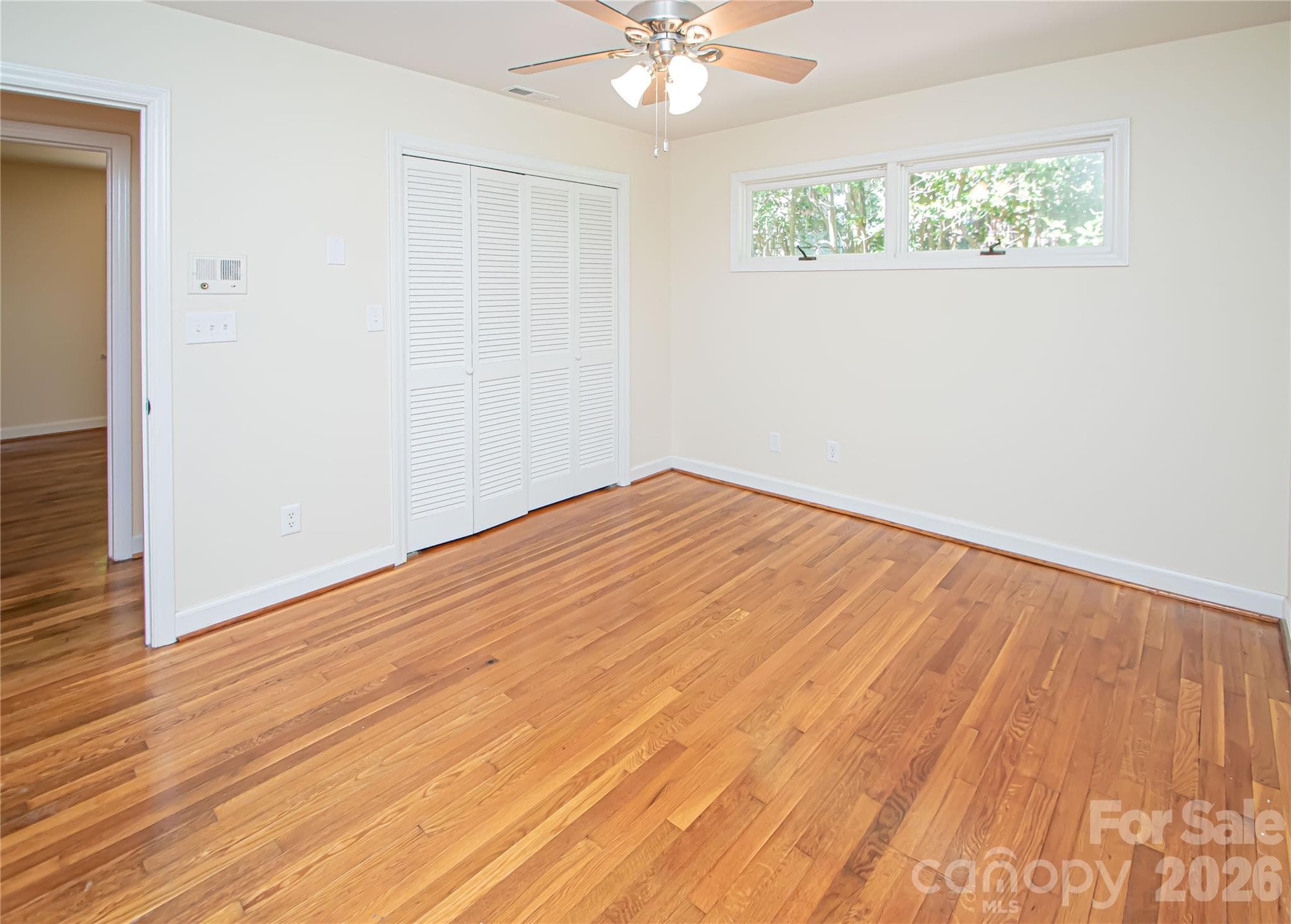 Spacious primary bedroom featuring beautiful hardwood flooring, a ceiling fan for climate control, and a generously sized closet. - 7400 Oakwood Lane, Charlotte