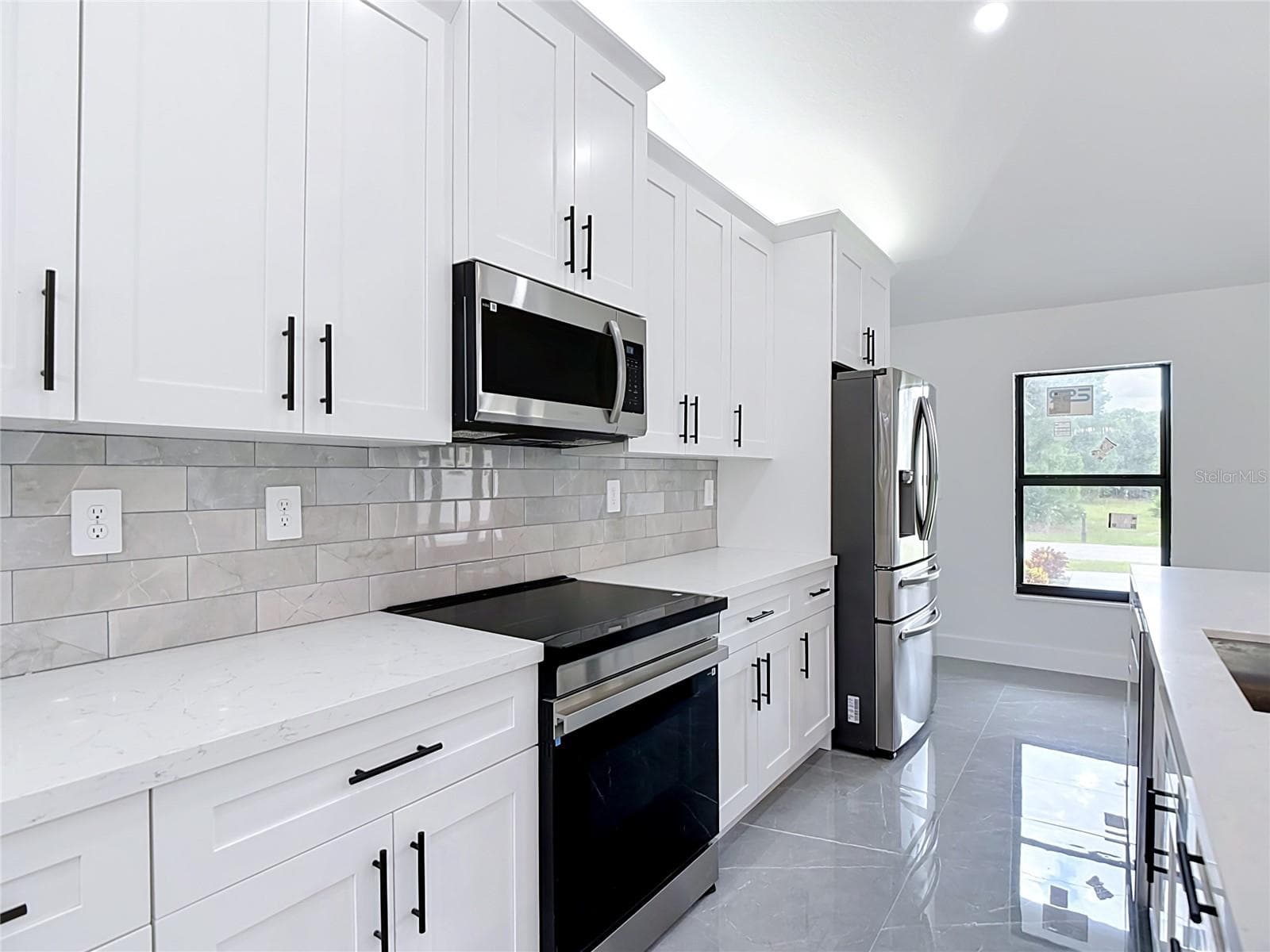 Gourmet kitchen features lighting above cabinets, quartz countertops, stainless steel appliances including an induction oven, microwave, dishwasher & refrigerator! - 3613 NW 47TH LN, CAPE CORAL