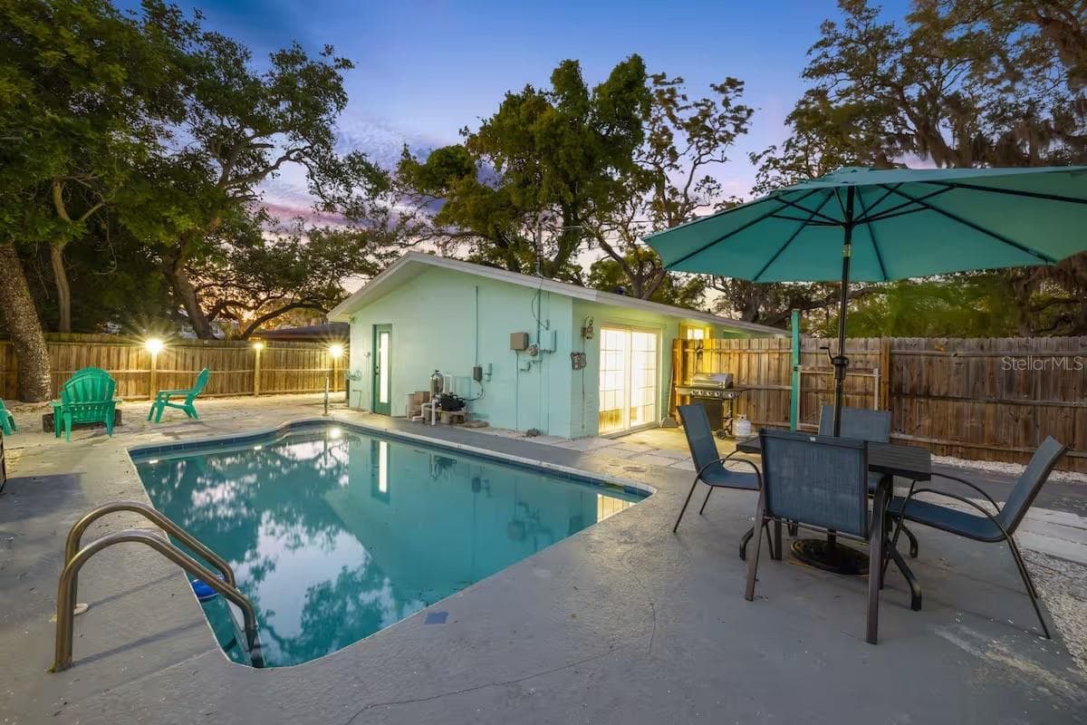 Evening lighting shows off the backyard’s resort-like setup, complete with heated pool, outdoor dining, BBQ area, and space to gather around the fire pit. - 201 SOUTH ST, PALM HARBOR
