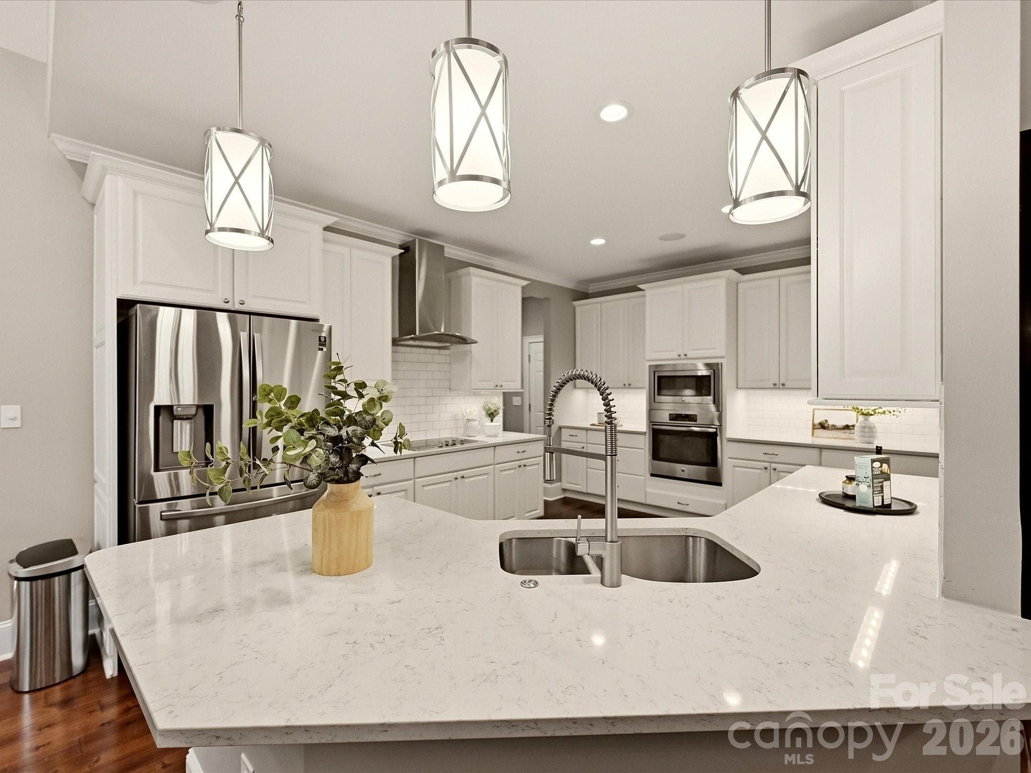 A bright, beautifully appointed kitchen features crisp white cabinetry, quartz countertops, stainless steel appliances, stylish pendant lighting, and an expansive island for  workspace or seating. - 3167 James Plantation Drive, Denver
