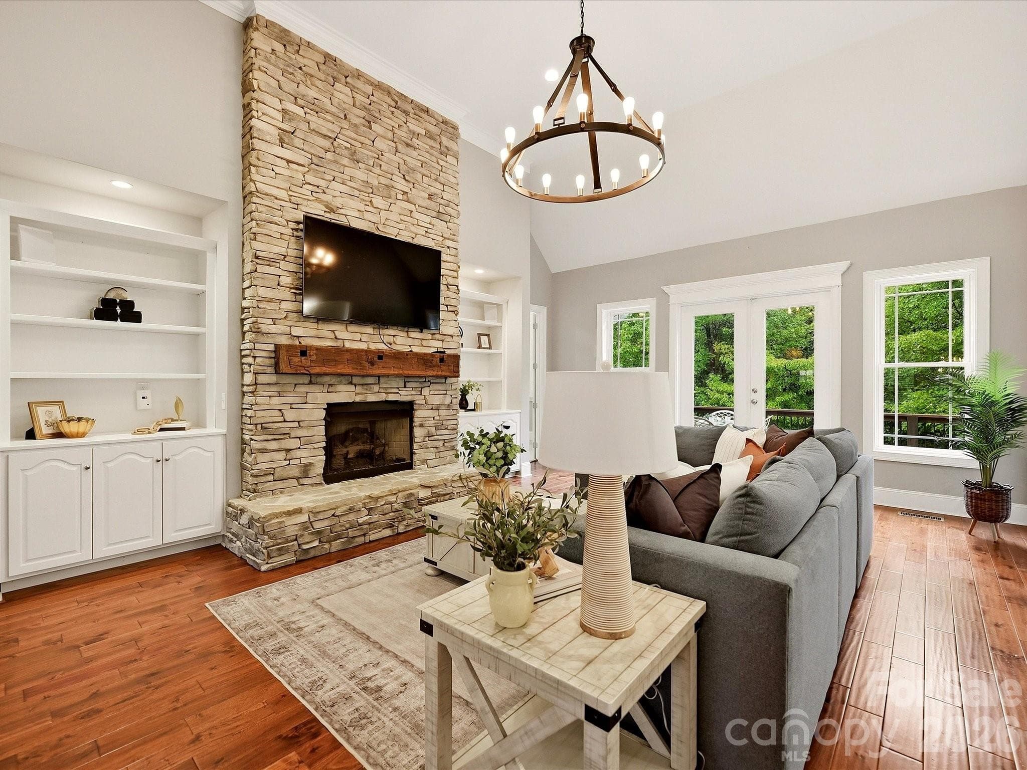A spacious Great Room showcases a dramatic floor-to-ceiling stacked-stone fireplace with a rustic wood mantel, custom built-ins, vaulted ceilings, beautiful floors, and abundant natural light. - 3167 James Plantation Drive, Denver